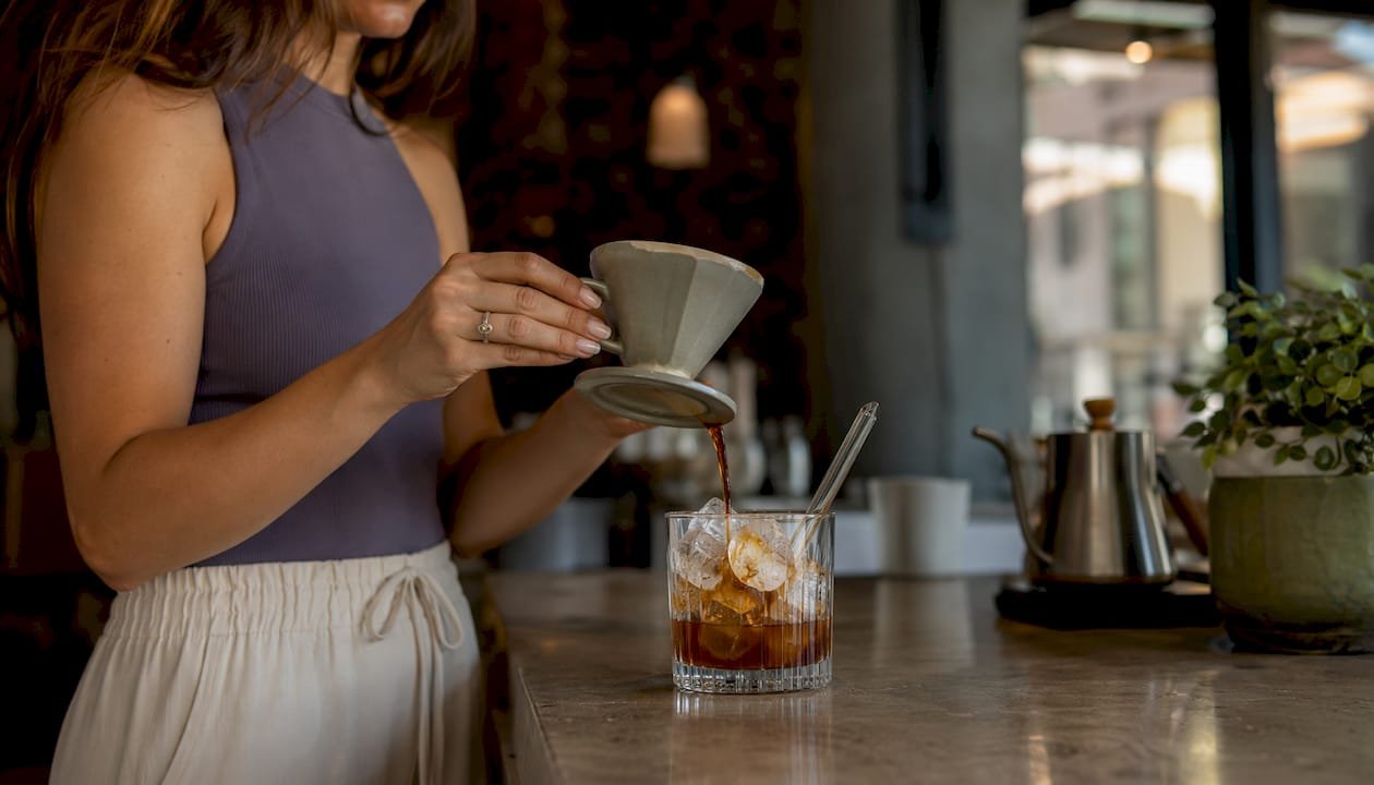 Hands pouring Vietnamese coffee over spoon into ice glass